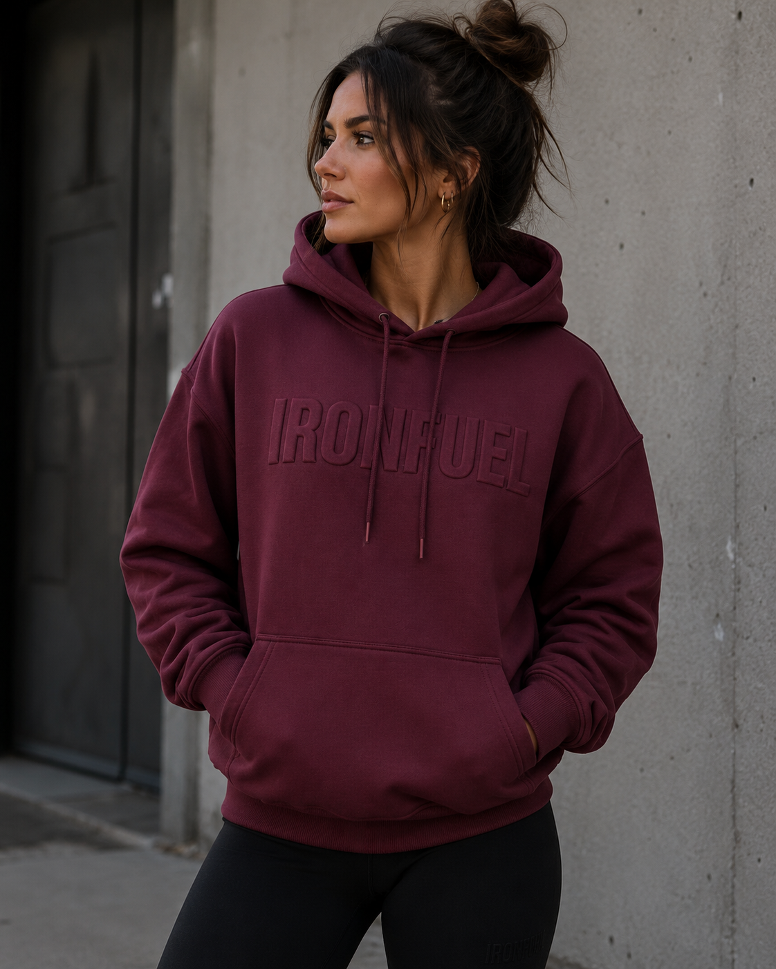 Woman wearing IRONFUEL burgundy hoodie against concrete wall