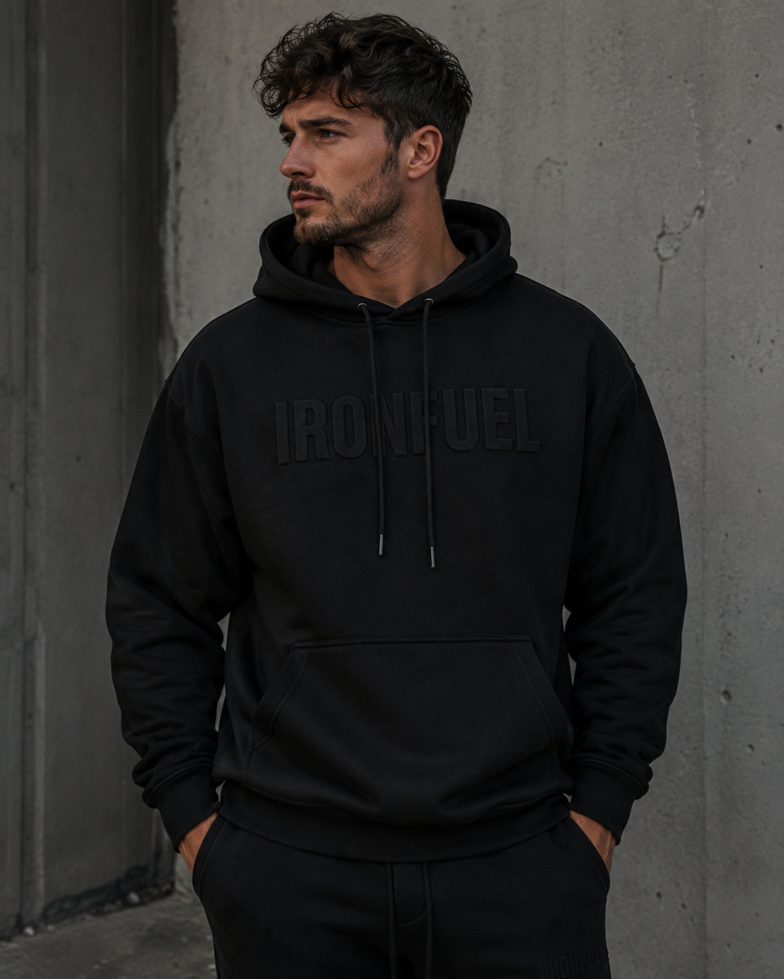 Man wearing IRONFUEL black hoodie against concrete wall
